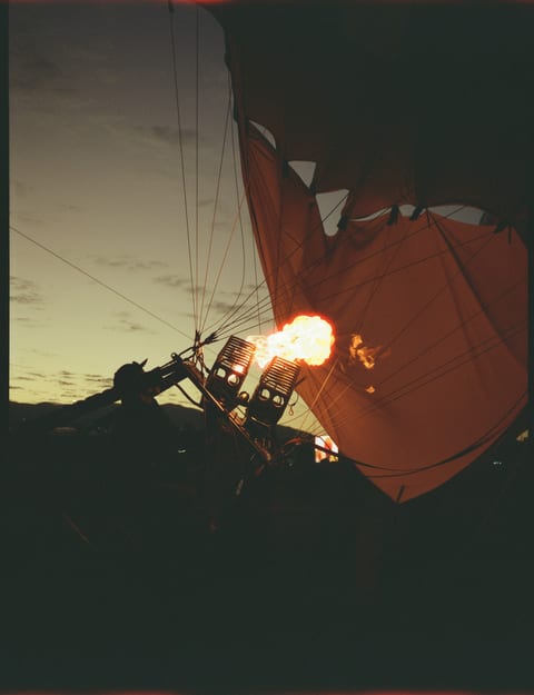 A hot-air balloon burner firing at dusk, the envelope lit orange