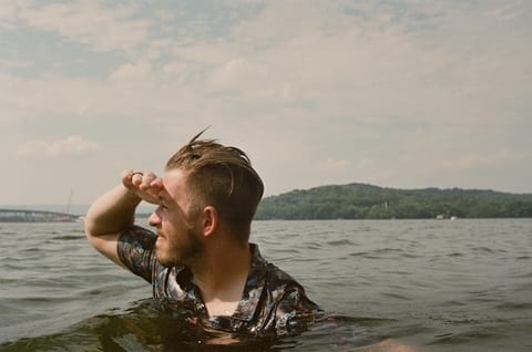 Kody, chest-deep in a river, shading his eyes against the sun